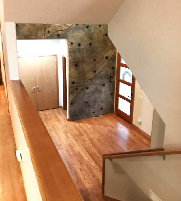 The base of a multistory climbing wall is visible in a home's foyer, near the base of the stairs