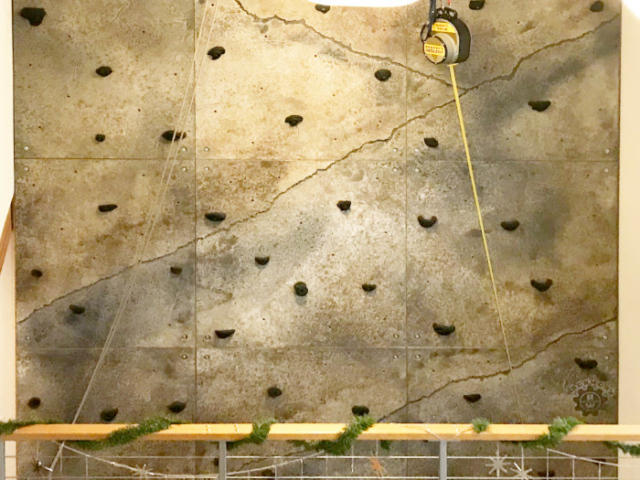 The upper portion of a climbing wall, including a rope setup, is visible from the landing on a home's staircase.