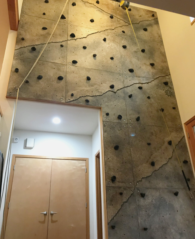 A multi-story climbing wall installed in a home's foyer is mounted around and above access to storage and other rooms.